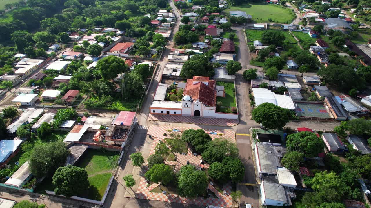 Toma con dron que captura una vista panorámica de una pequeña comunidad rural con su iglesia central y casas tradicionales ubicadas entre exuberantes colinas verdes