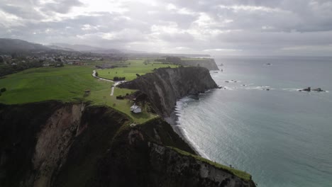 backwards aerial establishment shot of a small hermitage surrounded by nature, ermita de la regalina, situated on the steep cliffs of the cantabrian sea in asturias, spain