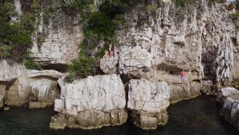 tourist cliff jumping into tropical mediterranean ocean cove, aerial