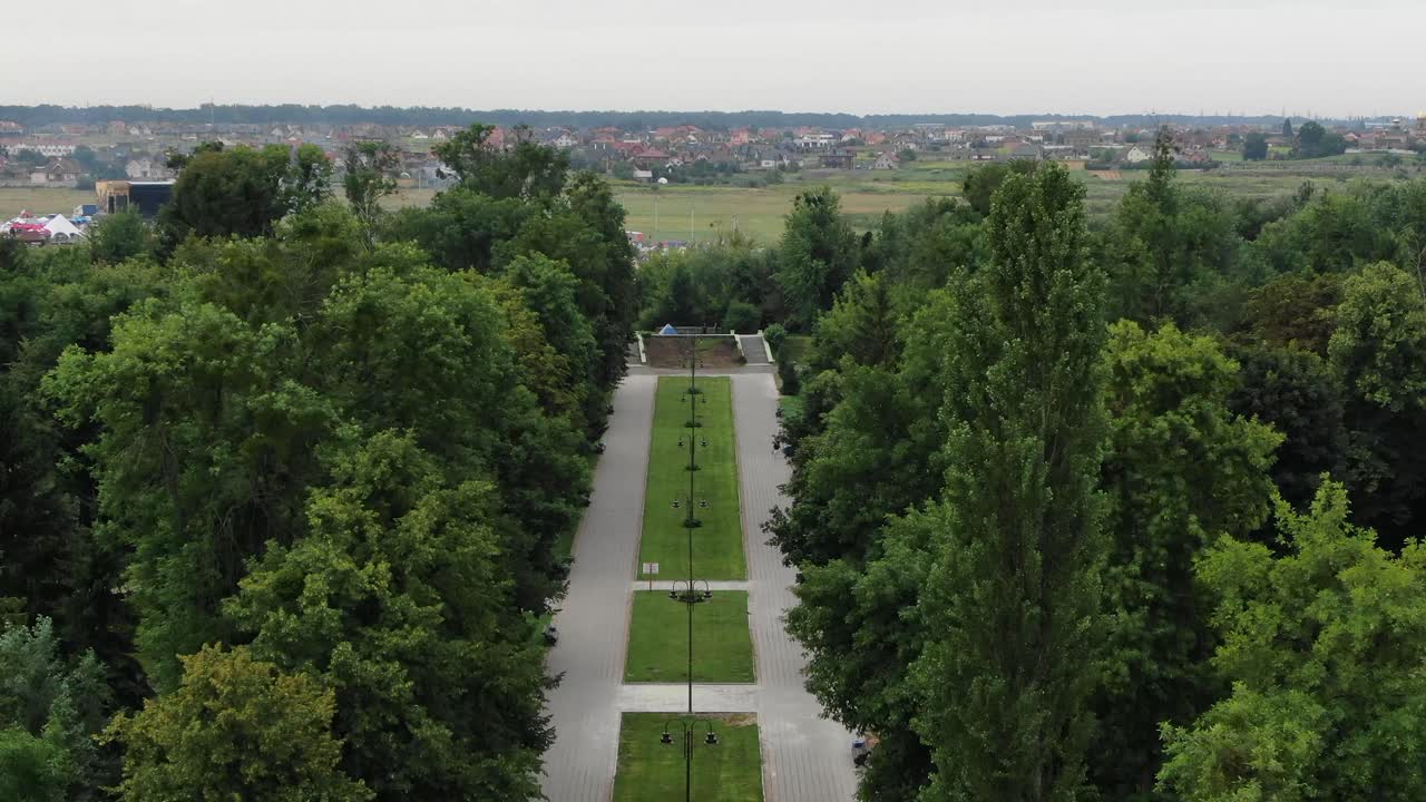 vista aérea de la acera atravesando un parque rodeado de árboles que conducen a un campo lleno de tiendas de campaña en un festival de música