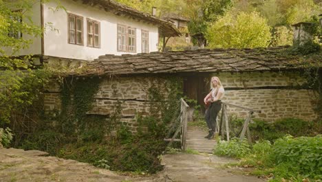 Beautiful-young-country-girl-strums-acoustic-guitar-village-scene-Bulgaria