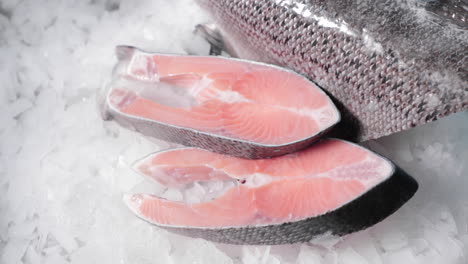 grandes trozos de salmón crudo en rodajas sobre hielo junto a medio trozo de pescado