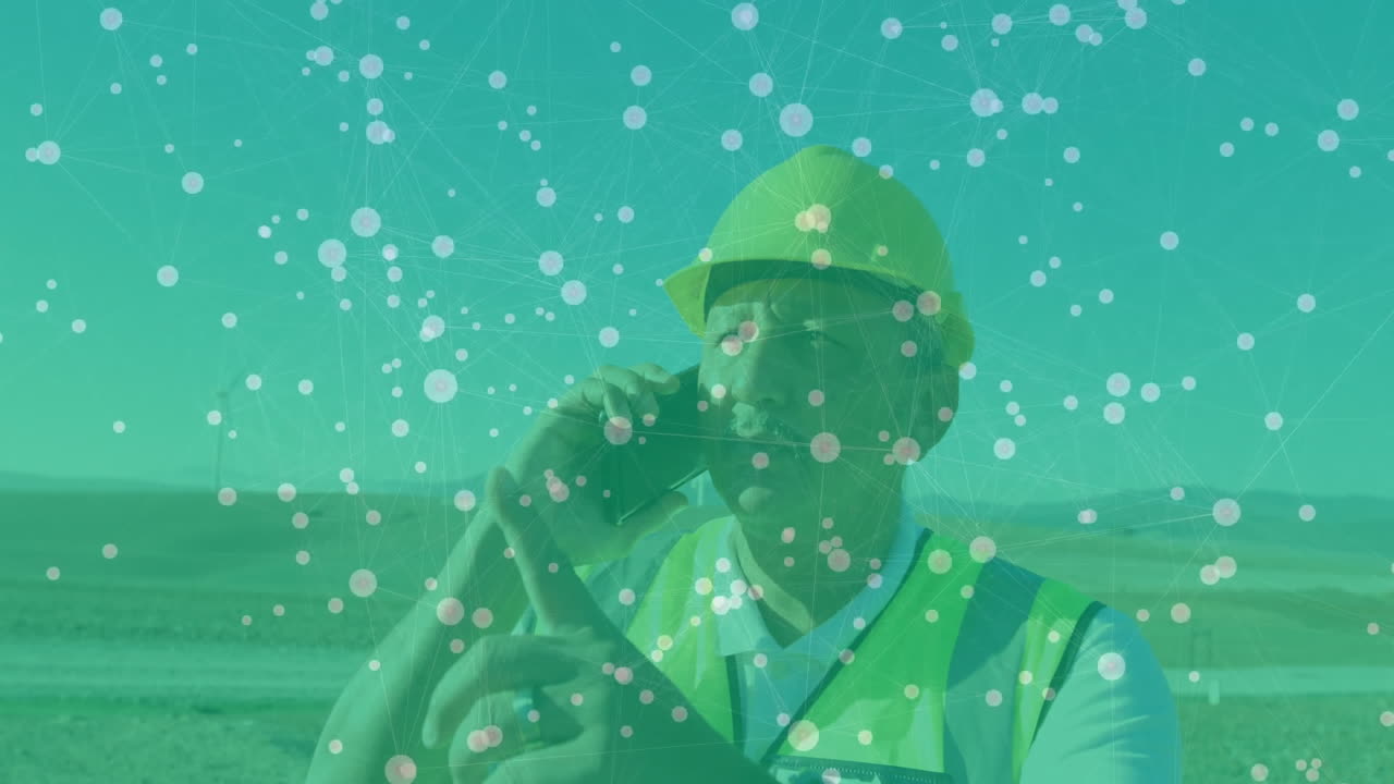 Wind energy technician talking on smartphone in wind farm field, showing digital network overlay