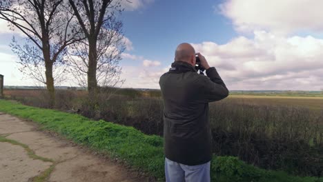 Footage-of-man-looking-at-countryside-with-binoculars,-this-footage-could-show-either-a-farmer-looking-over-his-fields,-or-a-birdwatcher