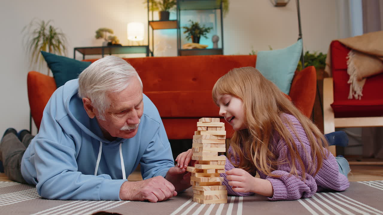 pequeña nieta linda emocionada jugando al juego de bloques de construcción con el abuelo sonriente en casa