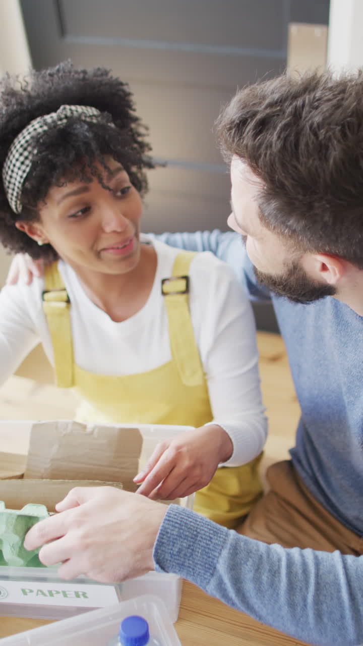Vertical video of happy diverse couple having fun preparing recycling at home, copy space