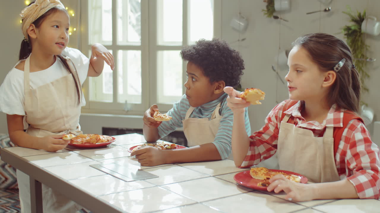 niños comiendo pizza y charlando en la cocina en la lección de cocina