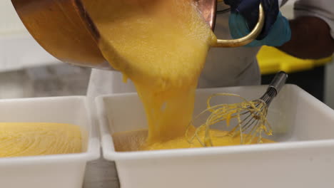 pouring hot custard cream into plastic baking pans - close up, panning right shot