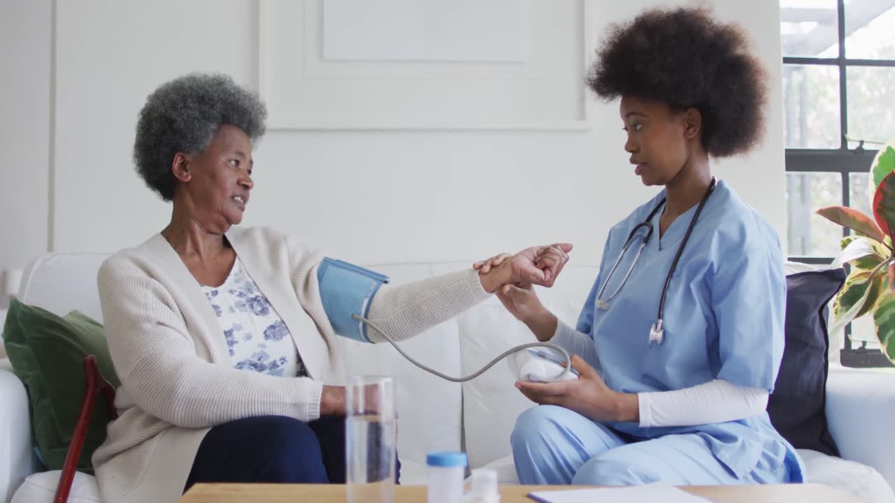 Caring african american female doctor checking blood pressure of senior female patient, slow motion