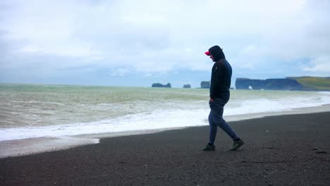 hombre caminando solo en la famosa playa de arena negra de reynisfjara en el sur de islandia