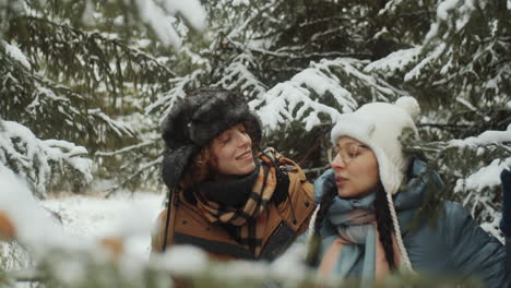 cheerful girlfriends walking and chatting in winter forest