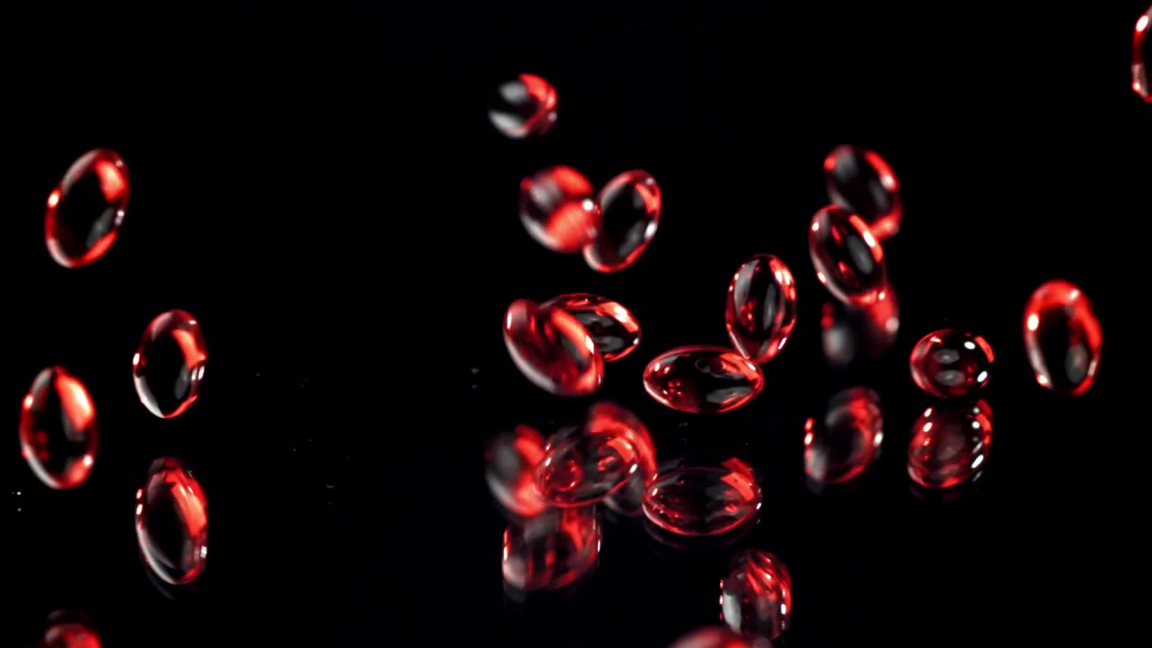 Red Gel Capsules Falling in Slow Motion on Black Surface