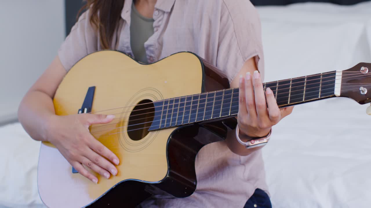 Mujer afroamericana empezando a digitar acordes cerca del clavijero, practicando guitarra acústica en la cama.