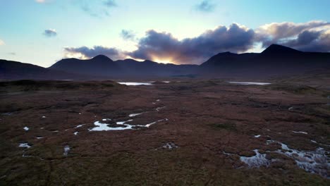 Drohnenaufnahmen-Aus-Der-Luft,-Die-Tief-Und-Nahe-An-Der-Oberfläche-Eines-Torfmoors-Fliegen,-Bevor-Sie-Aufsteigen,-Um-Bei-Sonnenuntergang-Süßwasserseen-Und-Dunkle-Berge-Am-Horizont-Zu-Enthüllen