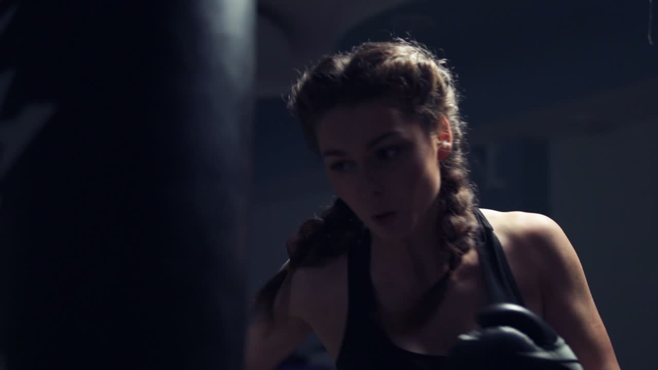 Beautiful young tanned woman punching bag in fitness studio. Boxing in Slow Motion