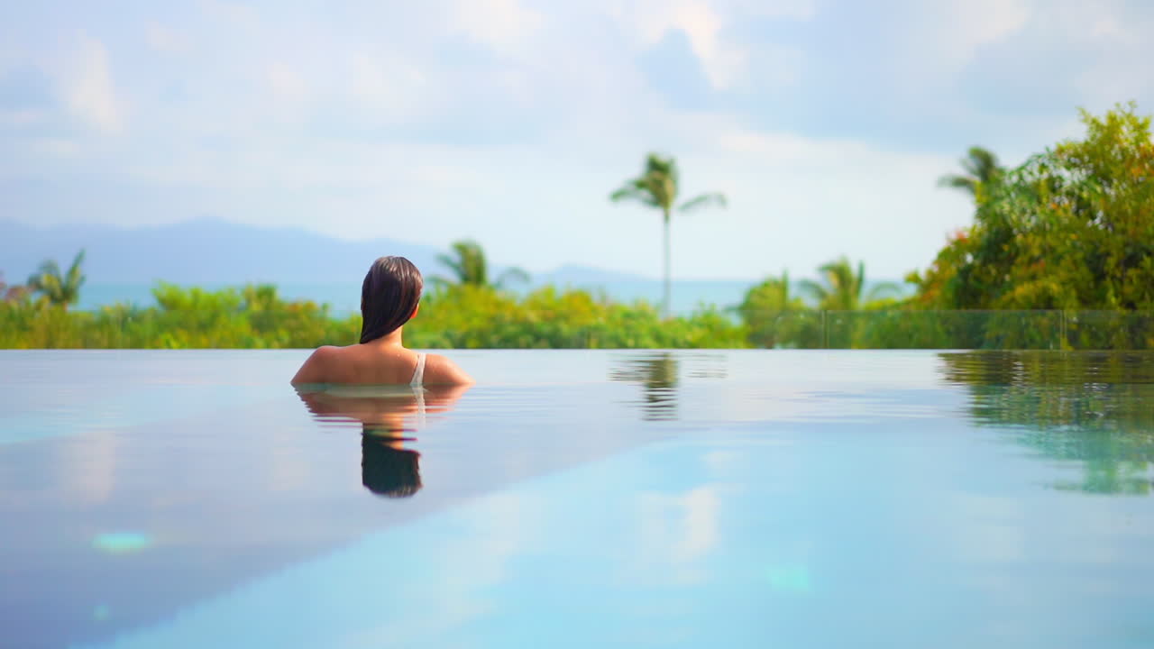 Rückansicht einer Frau in einem Infinity-Pool mit Blick auf das Panorama