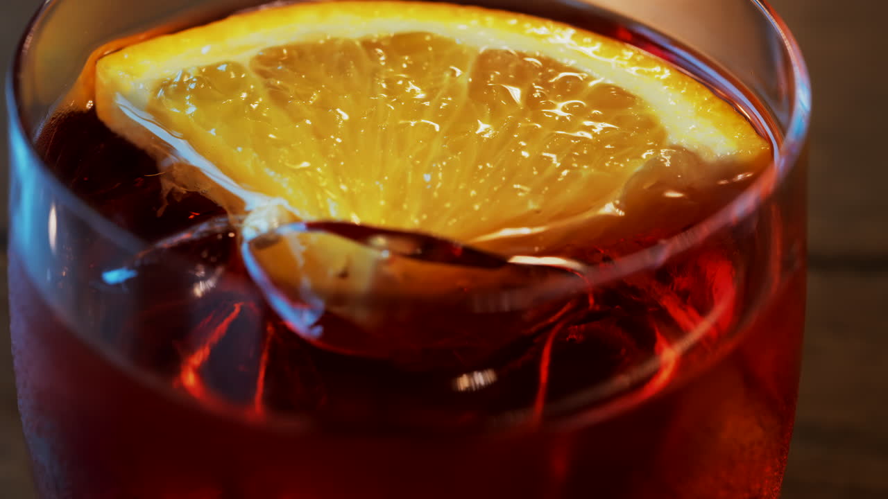 Primo piano di un cocktail Negroni con fetta d'arancia e cubetti di ghiaccio su un tavolo di legno