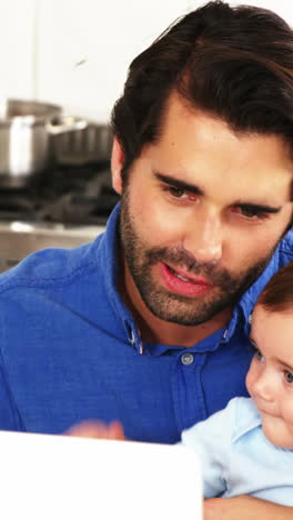 padre feliz sosteniendo a su bebé y usando una computadora portátil