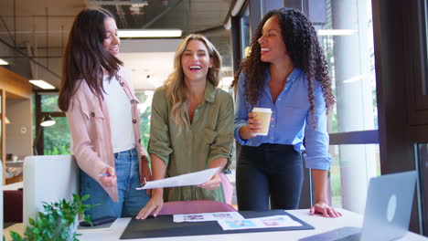 Female-Business-Team-Meeting-At-Desk-In-Open-Plan-Office-Approving-Checking-Proofs-Or-Design-Layouts