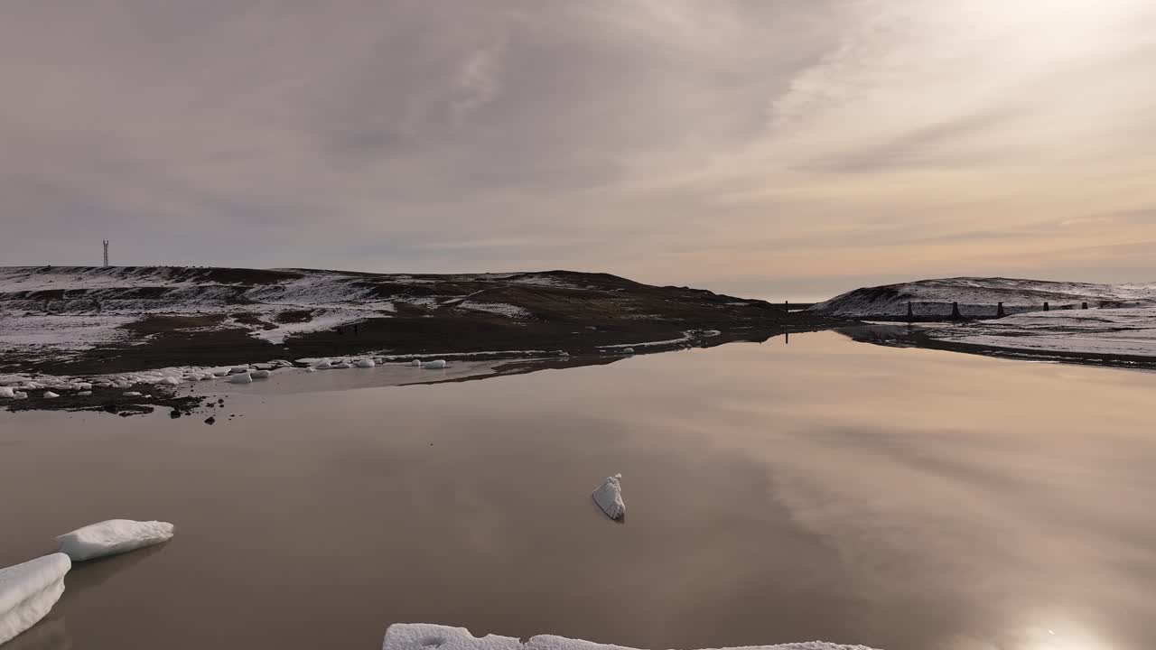 Iceland’s Fjallsárlón Glacier lake - smooth drone flight during golden hour with peaceful icy reflections, soft sunset sky and tranquil winter landscape.