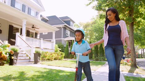 mother walks with son as he rides scooter along sidewalk