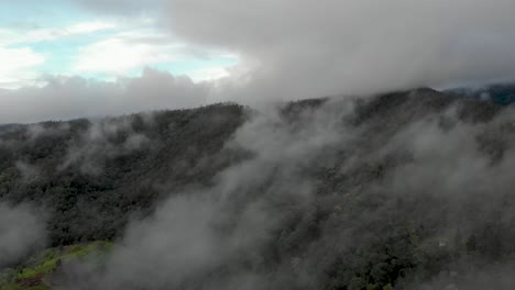 cinematic aerial drone shot flying through misty cloud cover on cold morning to reveal mountainous hillsides among quiet countryside in north thailand