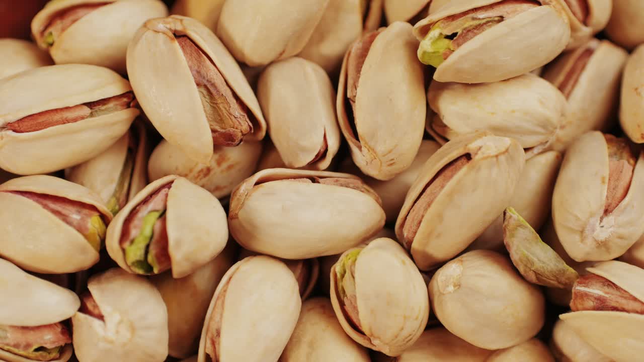 Salted pistachios on plate close-up macro. Nuts snacks for parties, fried crispy pistachios with cracked shells for beer . High quality 4k footage