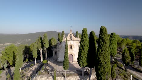 nivel frontal que se acerca a una pequeña torre campanaria en la parte superior de una ermita de naves en la parte superior de una colina entre los árboles en españa