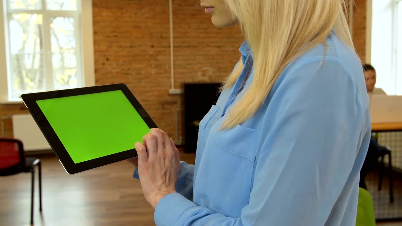 близкий взгляд на молодую привлекательную женщину, использующую черный планшет с зеленым экраном в современном офисе.