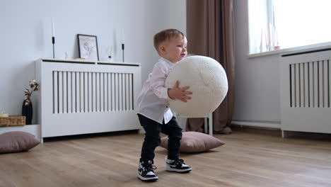 adorable toddler picking up a round white cushion from the floor. happy caucasian child playing cheerfully at home.