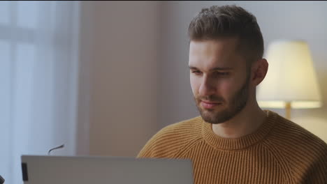 Männlicher-Benutzer-Arbeitet-Mit-Laptop-Und-Setzt-Eine-Brille-Zur-Korrektur-Der-Sehkraft-Auf,-Surft-Abends-Zu-Hause-Im-Internet,-Porträt-Eines-Jungen-Mannes-Im-Zimmer