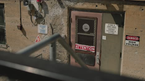 grungy exterior of a industrial hydro electric complex with danger high voltage warnings on the exterior near the door