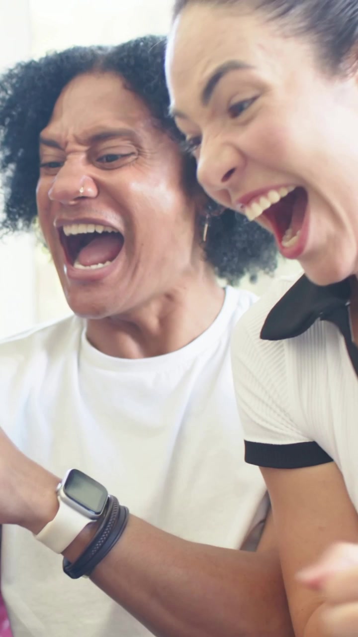 Video vertical: Reaccionando al teléfono, dos adultos apoyados en el sofá, animando, con camisetas blancas