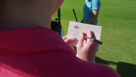 two caucasian women playing golf one writing in a notebook