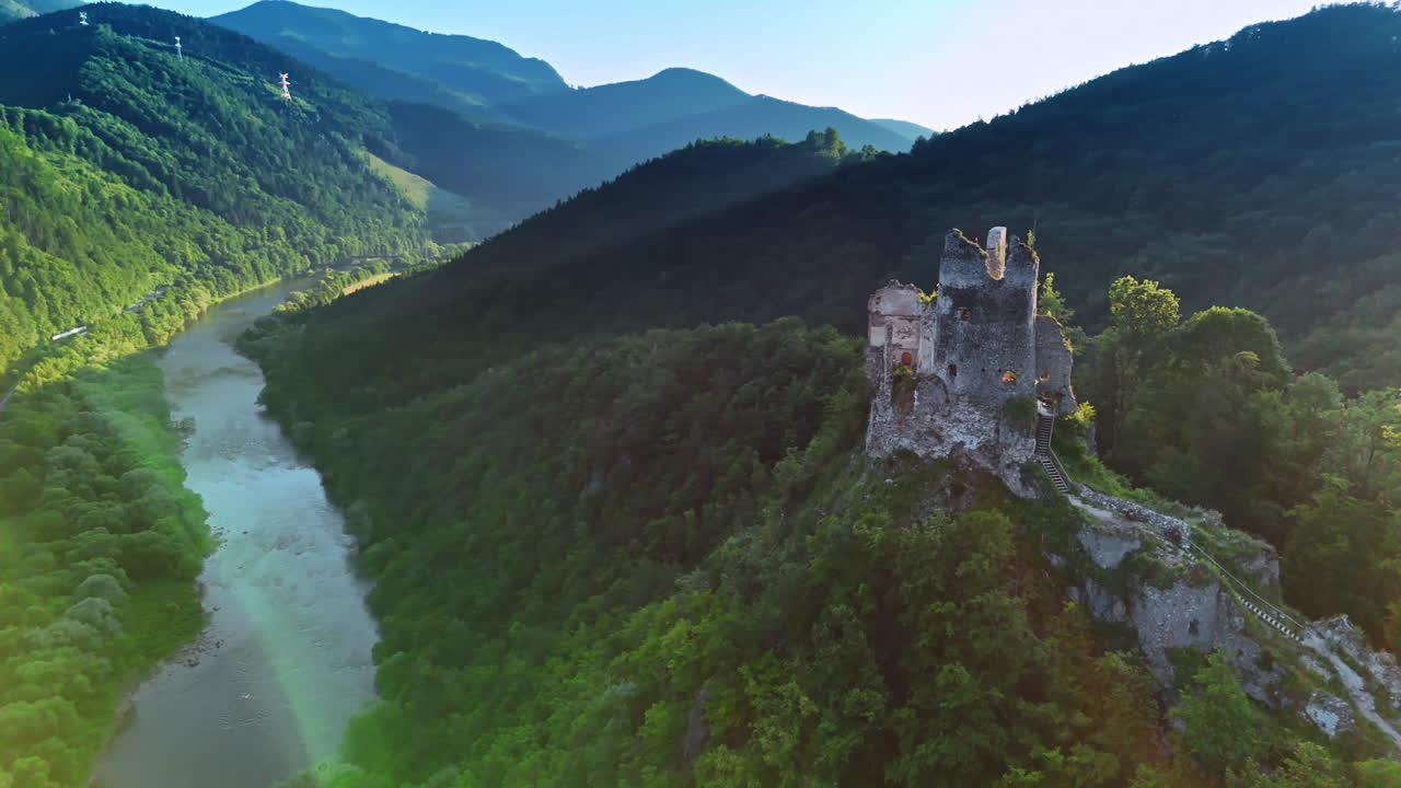 Rock over the mountain with ruins of the old castle on top. Spectacular mountains covered with lush forests and river around. Aerial view.