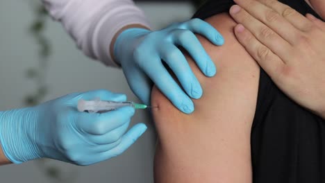 primer plano de una enfermera inyectando la vacuna en el brazo del paciente y luego limpiándola con una gasa estéril