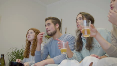 friends watching tv, drinking beer and supporting team at home