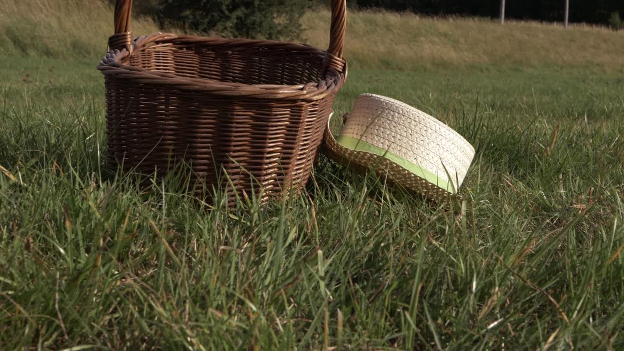 Straw hat and woven basket in a field zoom in shot