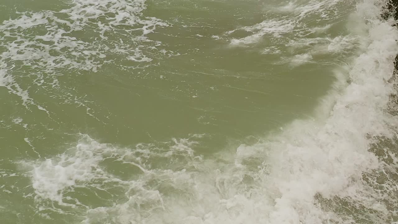 Aerial tilt-up shot of sea water hitting rocks in slow motion