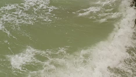 Aerial-tilt-up-shot-of-sea-water-hitting-rocks-in-slow-motion