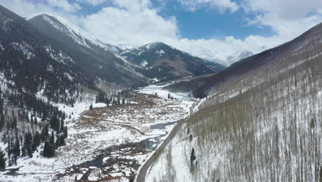 Road-in-between-two-mountain-ranges-in-winter-season-during-snowfall,-aerial-drone-view