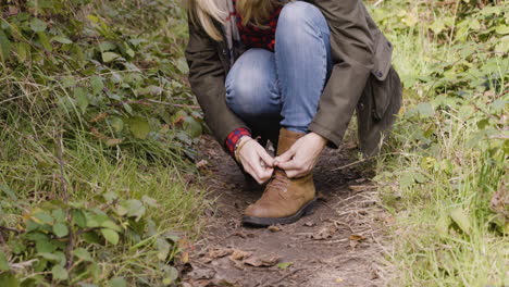 woman tying shoelace on forest path