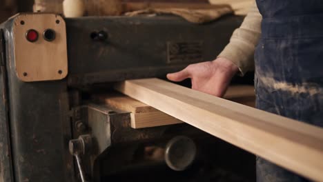 a man works in a carpentry shop. he goes to the grinding machine and installs a long rail into it. back view