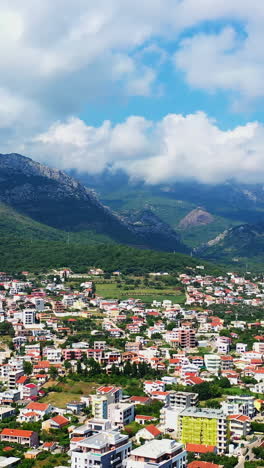 densely built low architecture of the city of bar in montenegro. white cloudscape covering the tops of the mountains surrounding the city. aerial view. vertical video