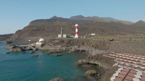red and white lighthouse on rocky shore with salt evaporation pools, fuencaliente