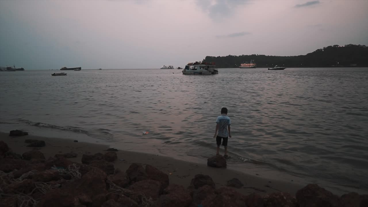 흥분한 어린 소년이 인도, 고아, 일몰에 마하다이 강둑을 따라 얕은 물에서 놀면서 위아래로 뛰어다니며 즐겁게 놀고 있습니다.