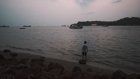 un joven emocionado saltando arriba y abajo divirtiéndose jugando en las aguas poco profundas a lo largo de la orilla del río mahadayi al atardecer, goa, india