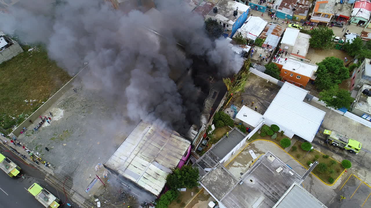 Aerial view overlooking a raging building fire, smoke rising while firemen quells the fire, in Rio de Janeiro, Brazil - pan, drone shot