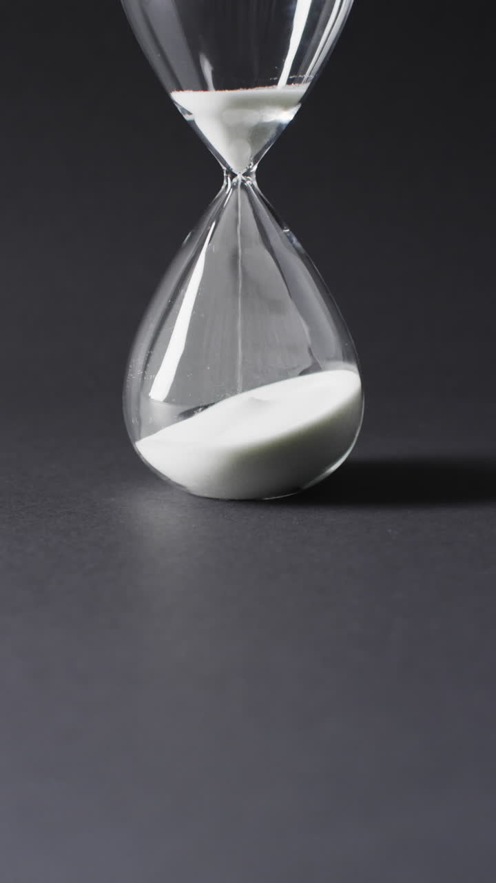 Vertical video of hourglass with sand pouring, copy space on black background
