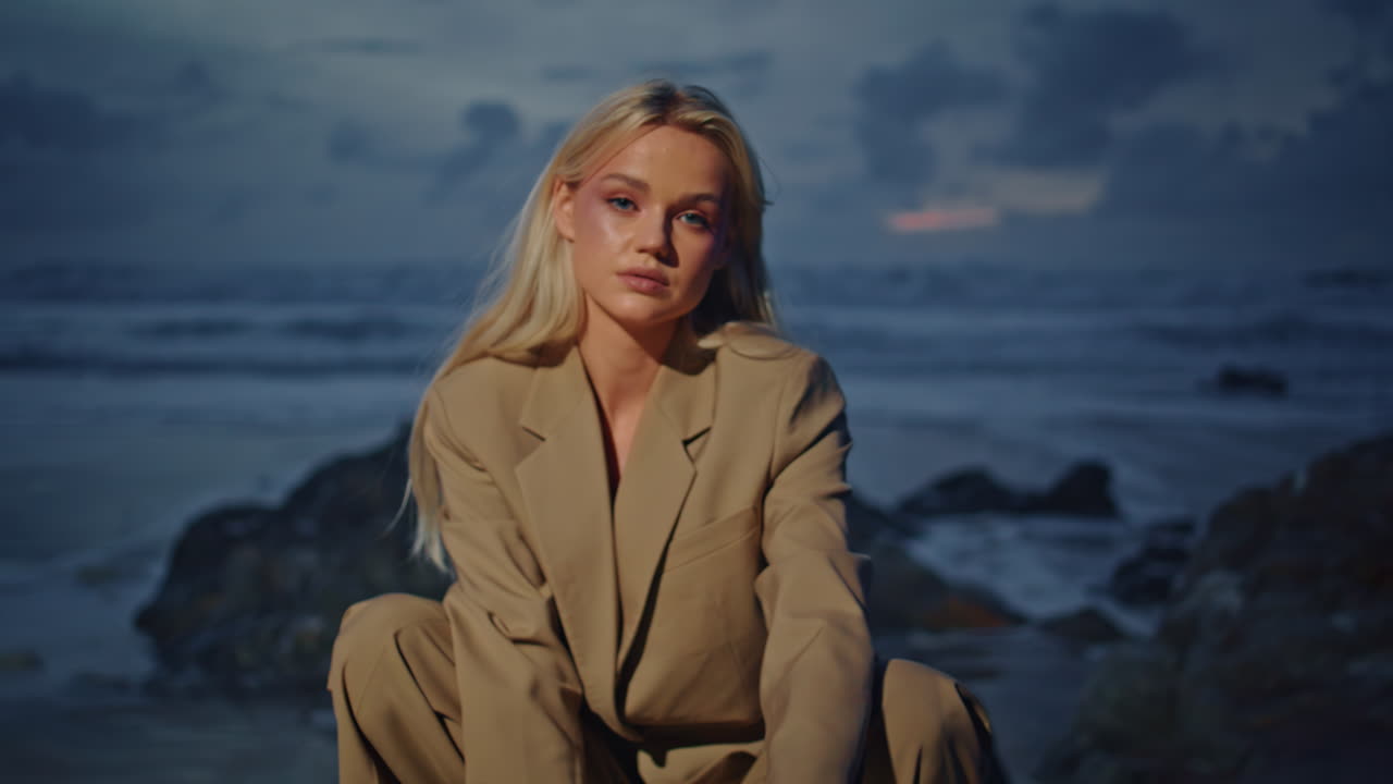 Closeup girl dusk beach looking camera. Attractive confident lady sitting rocks